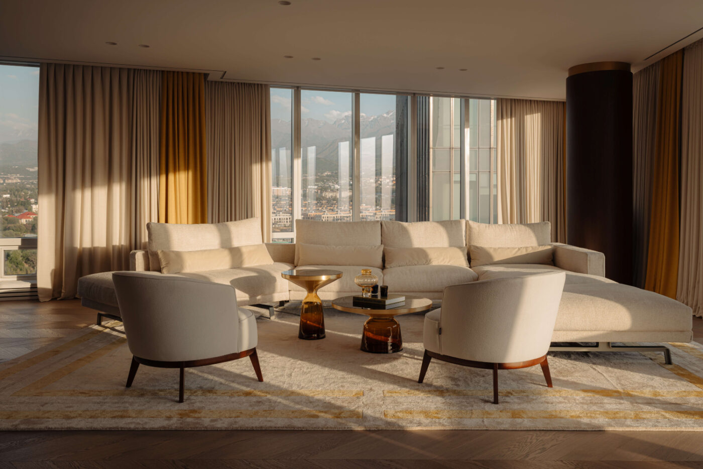 A bright living room with a large window illuminating a cosy, expansive sofa. Project by Akka Interiors.
