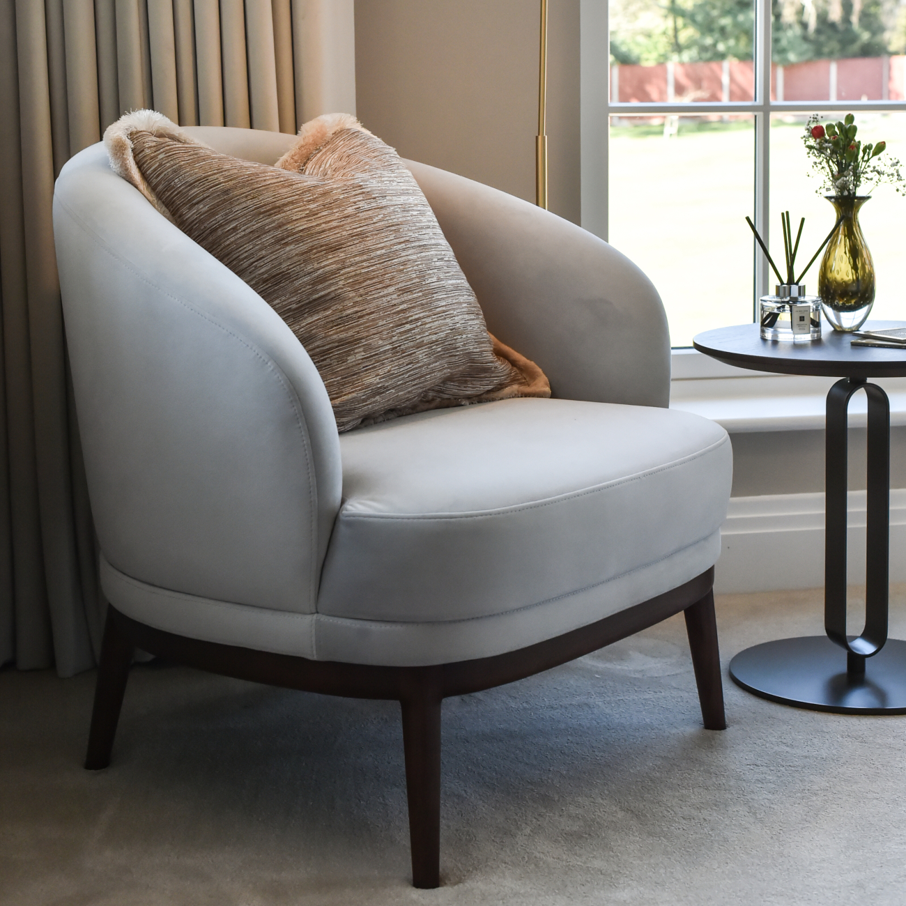 A simple armchair and table set against a window, creating a serene spot for reading or enjoying the view in a master bedroom design.