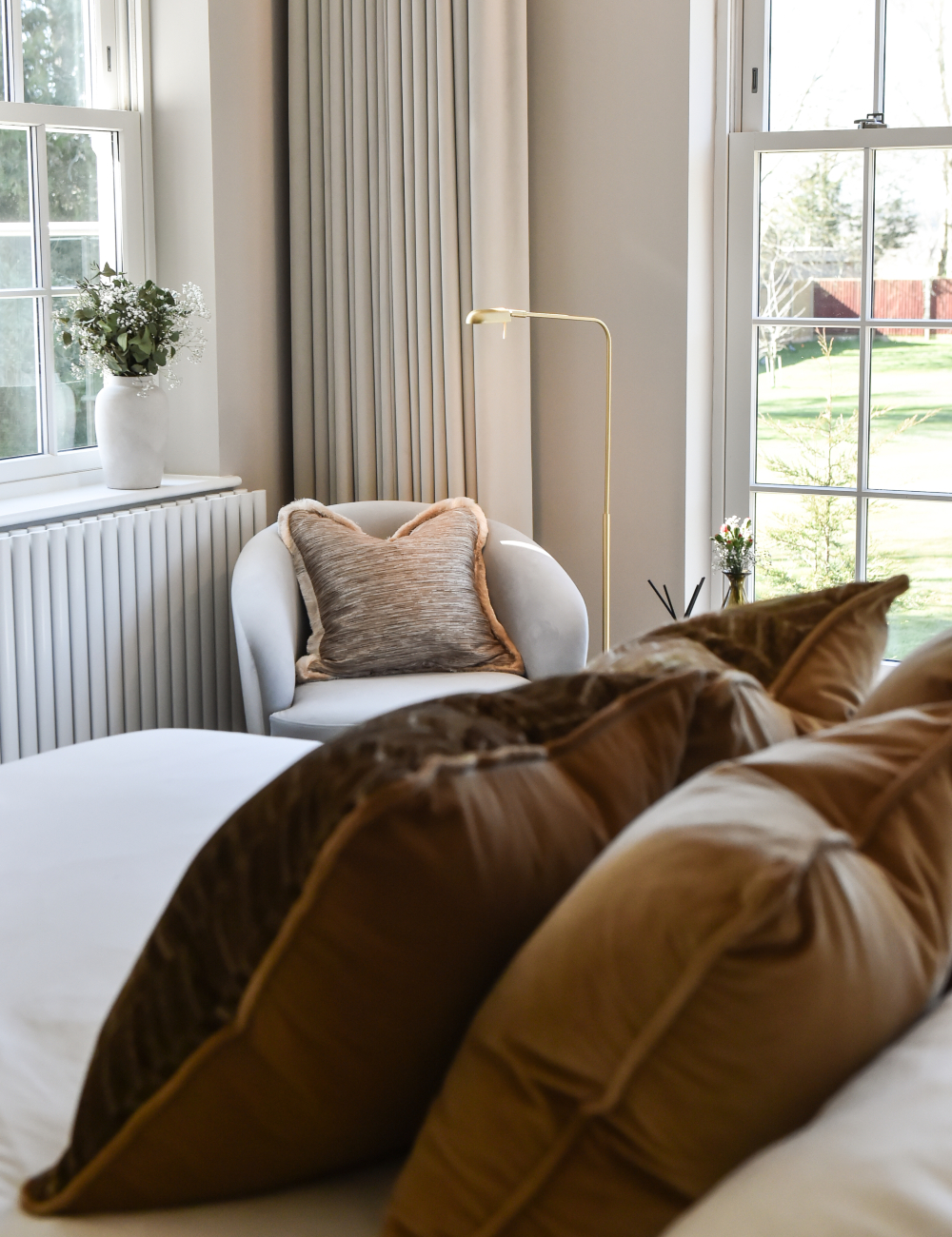 A tranquil master bedroom design scene with a bed, a chair, and a window that offers a view outside.