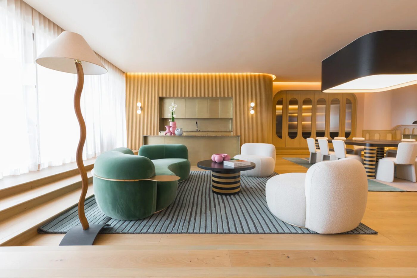 Andrés Gutiérrez project Modern living space with a green sofa, white chairs, and a striped rug. A wavy floor lamp stands by large windows, creating a warm, inviting ambiance. By one of the best mexican interior designers.