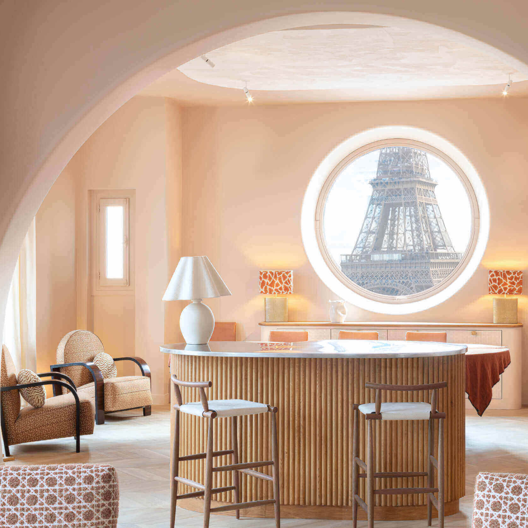 An Anne-Sophie Pailleret project in salmon tones with wood accents in the balcony and chairs. With a round window with a view to the Eiffel Tower.