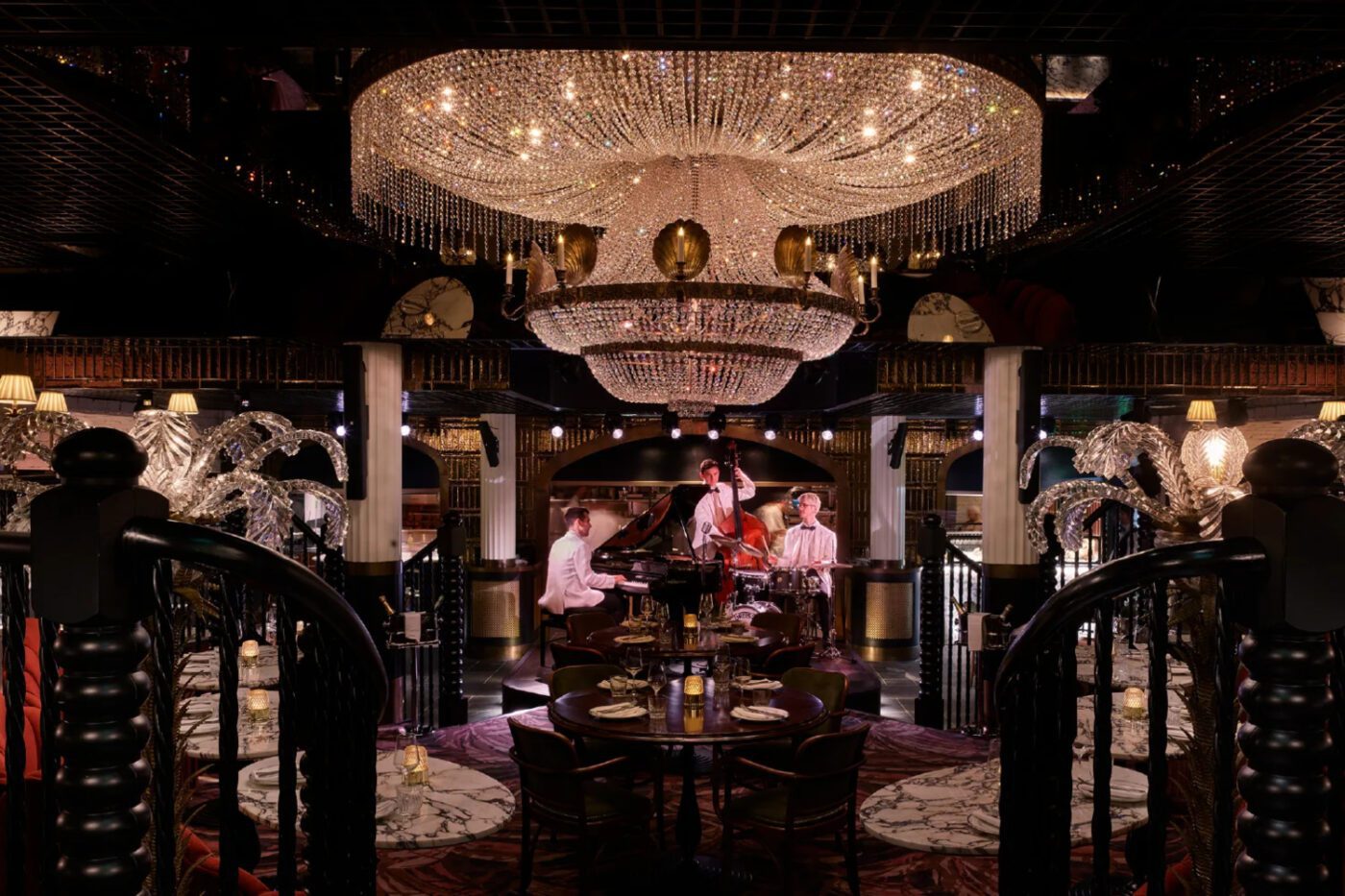 Artboard The Maine Restaurant Elegant restaurant interior with a grand chandelier, live jazz band performing under soft lighting. Marble tables are set for dining, exuding a luxurious ambience.