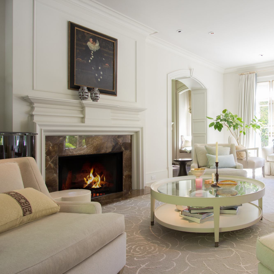 Living room with white tones and a fireplace in brown stone. With four white armchairs and a coffee table in white metal.