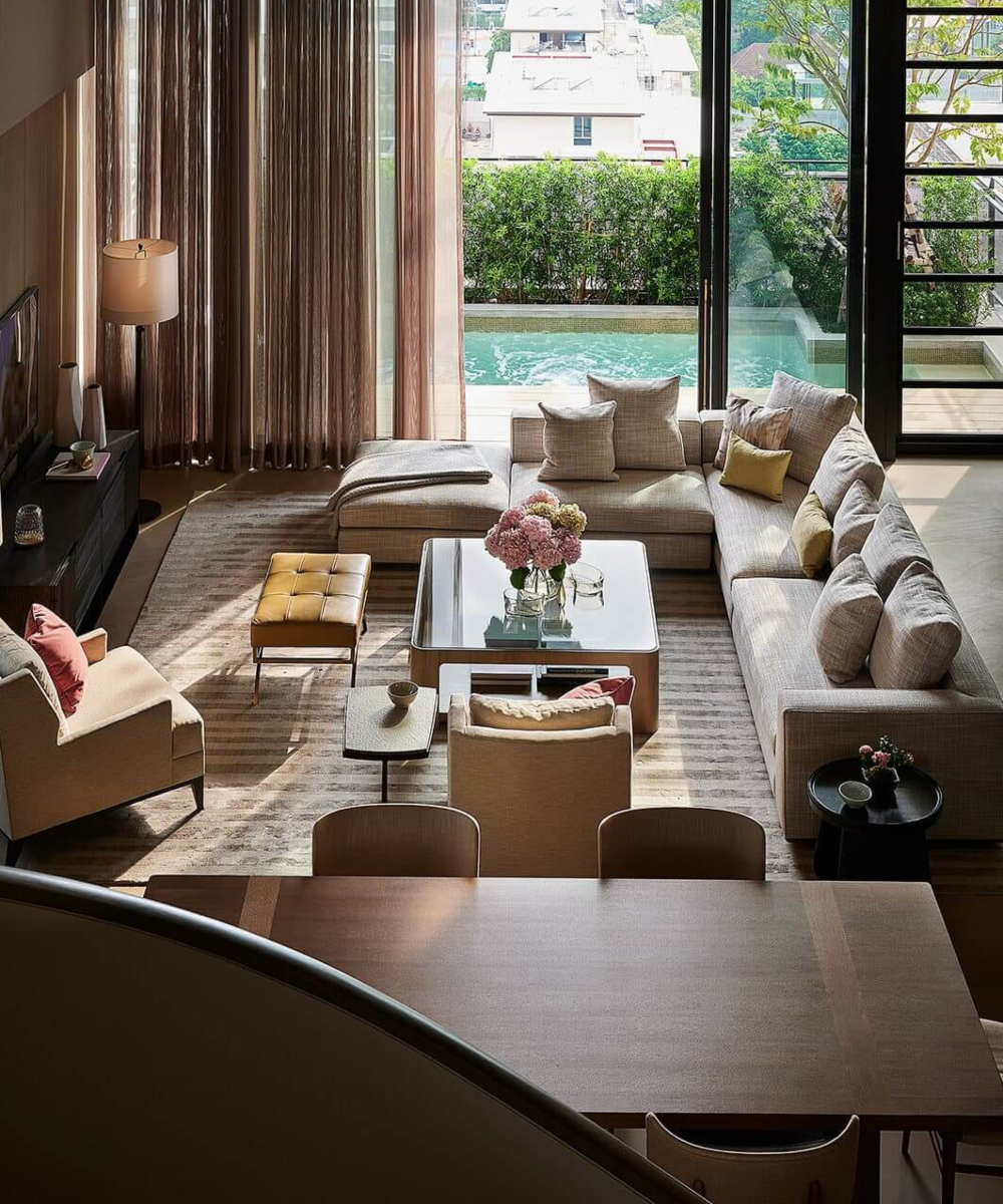 Barbara Barry - Best Interior Designers In the us (1) A modern living room with a floor-to-ceiling glass wall providing a scenic view of the pool area. By Barbara Barry