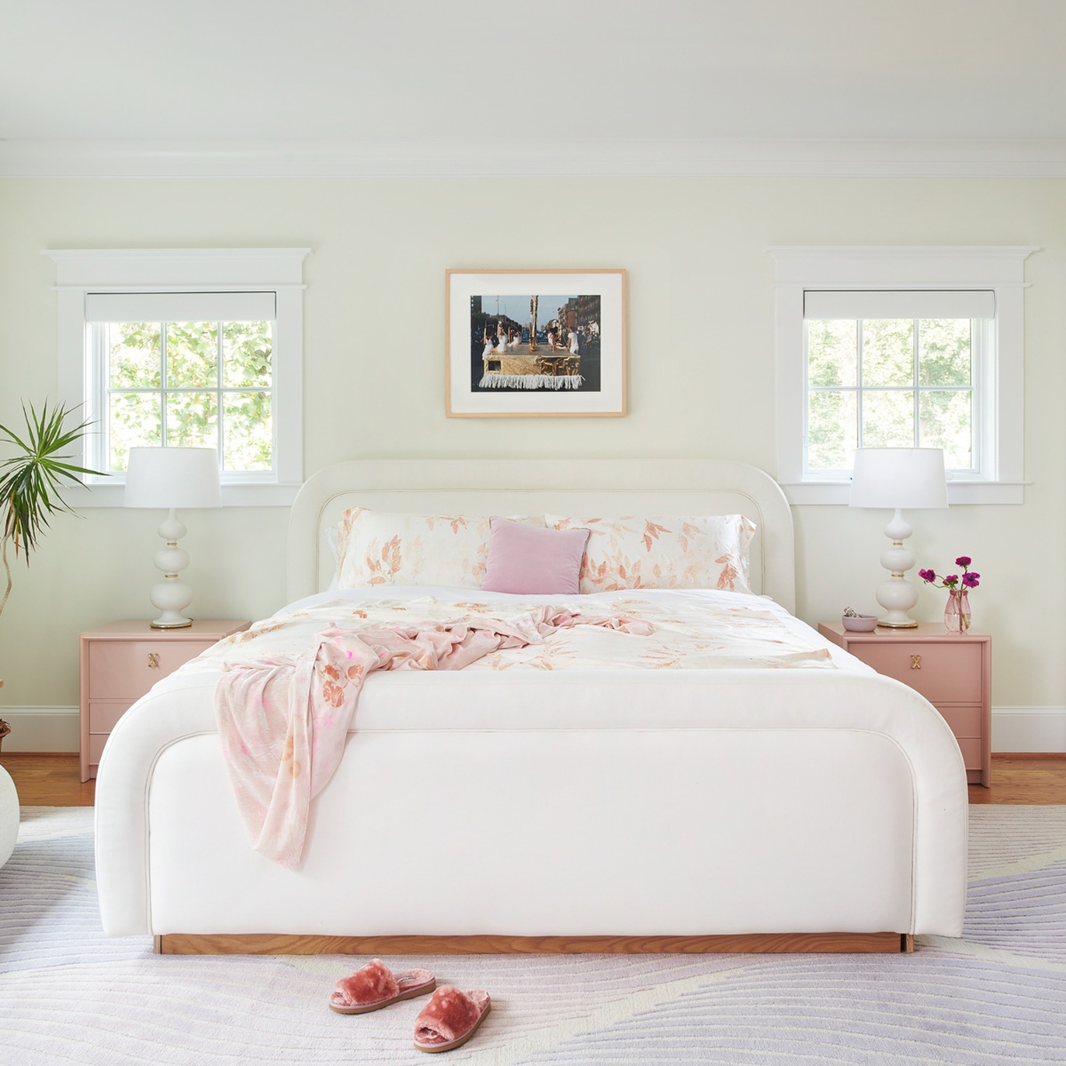 Bedroom in white colours. The bed, the carpet and the walls are white and the bedside tables are light pink.