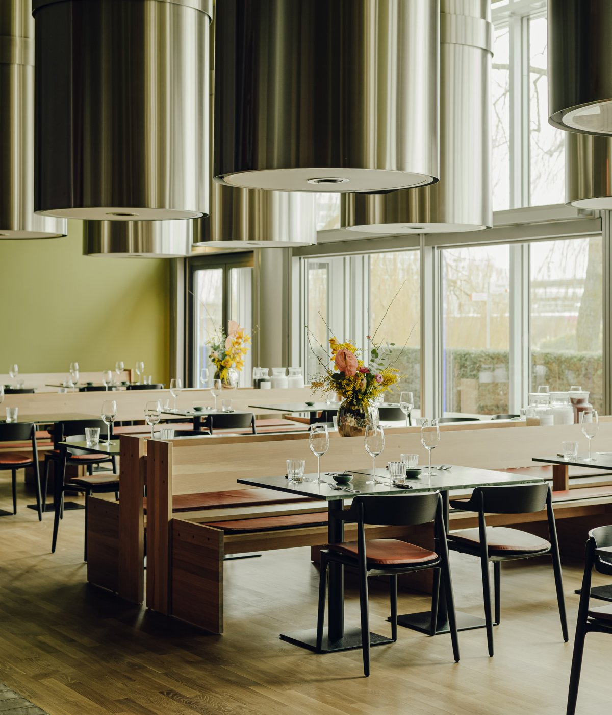 Restaurant with metal chandelier on the ceiling and wood furniture. The dining chairs are in black and there are wood benches.