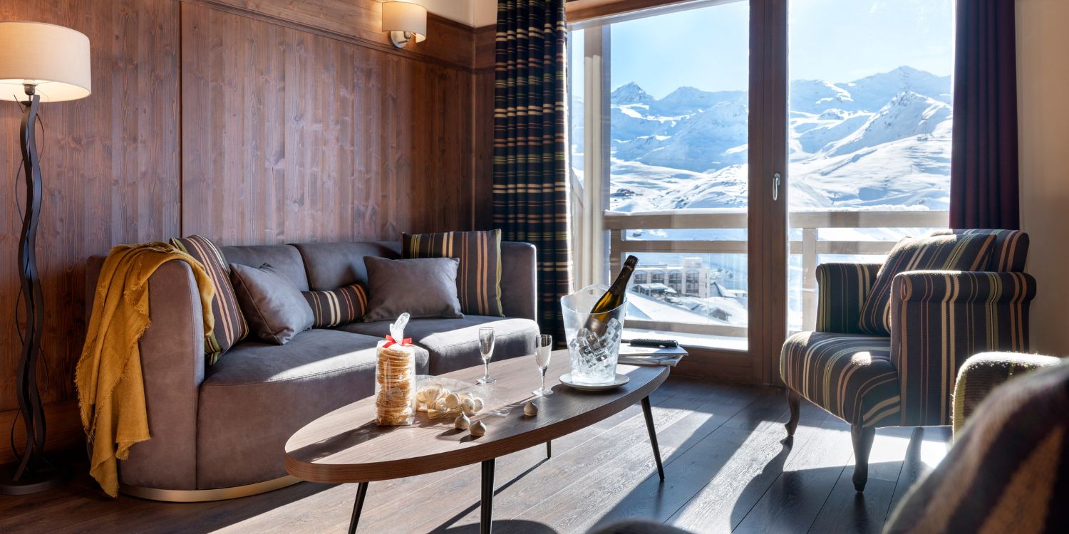 Bright living room with comfy furniture and panoramic views of majestic mountains outside. From the hotel Le Hameau du Kashmir in the French Alps.