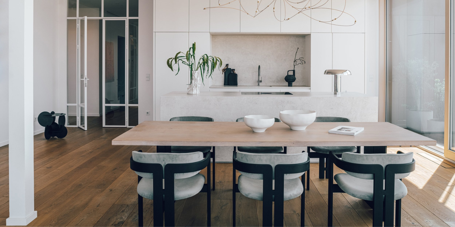 dining room project with six dining chairs in black wood and light blue fabric. With a dining table in light wood and a white kitchen island at the back. By one of the best interior designers in germany.