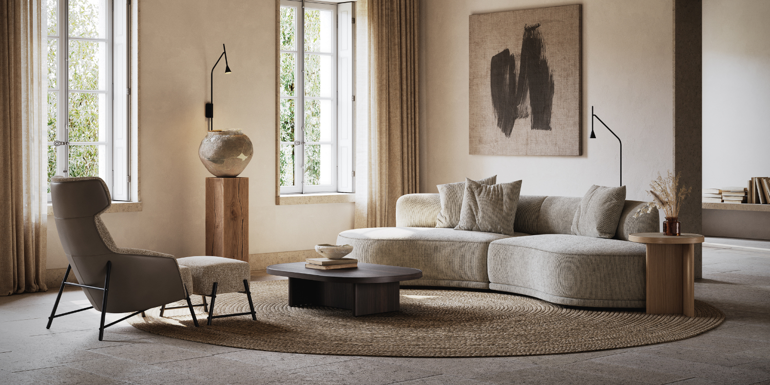 A modern living room with a curved beige sofa, round coffee table, and a high-backed chair with an ottoman. Large windows let in natural light, and a textured abstract artwork hangs on the wall. Neutral tones and a woven rug complete the serene look.