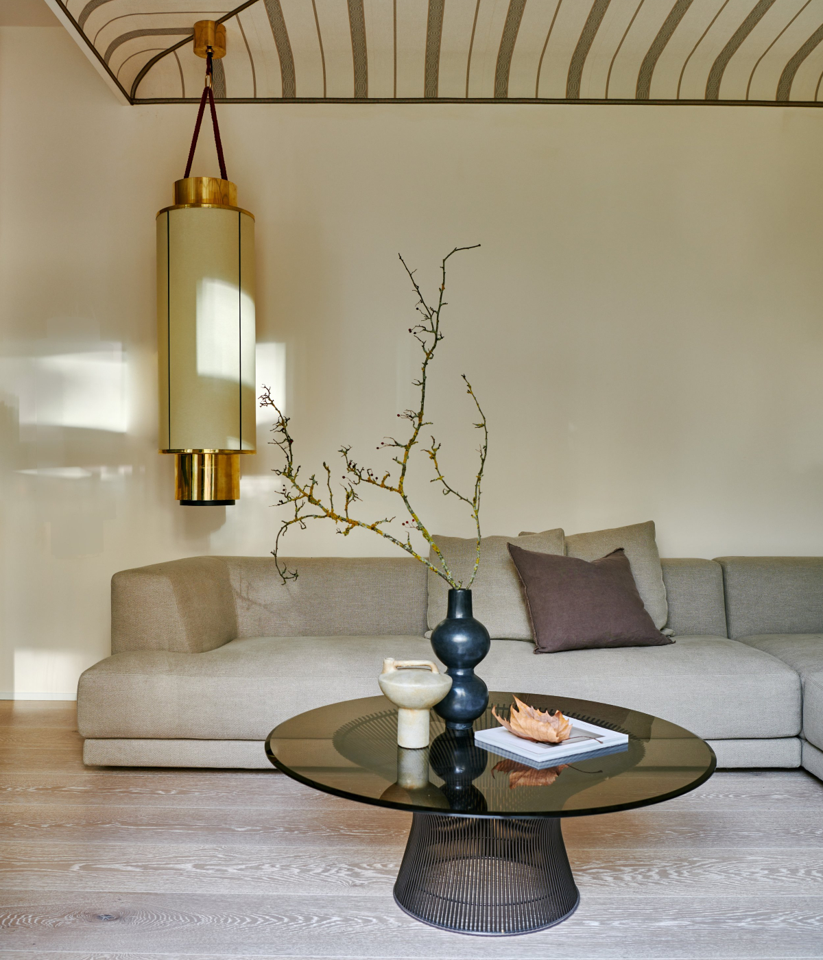 Living room in a modern aesthetic. With a round and long chandelier in gold and beige. The sofa is in beige and has a coffee table in the centre in black and glass. By one of the best interior designers in germany - Carlo Berlin.