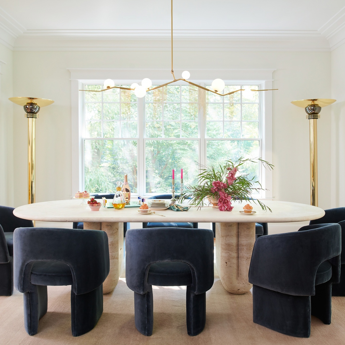 Dining room with navy blue dining chairs and white marble dining table. With gold accents at the lighting.