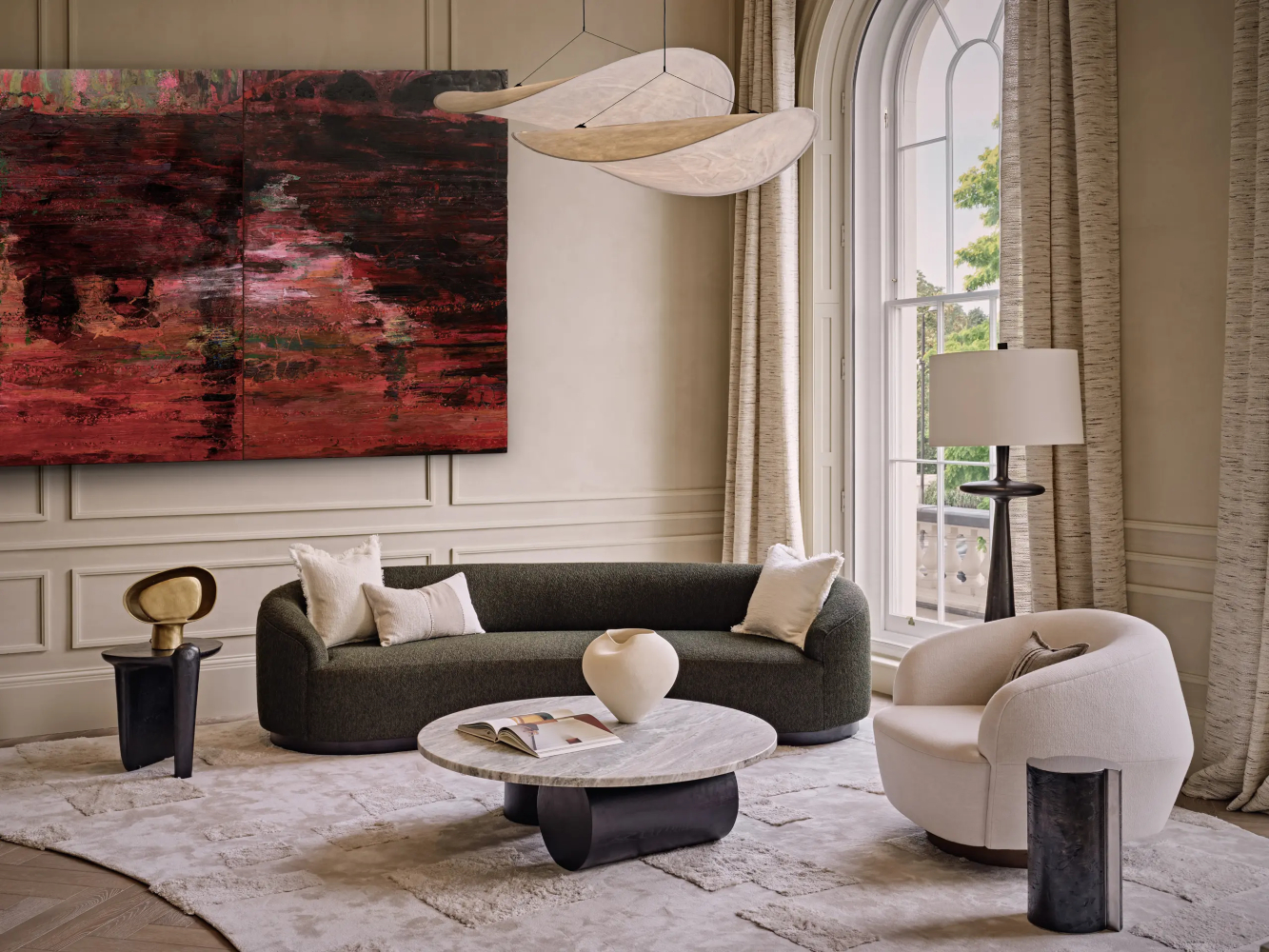 Living room project by Elicyon with a dark sofa and a white armchair. At the centre has a coffee table with a black base and a top in marble. On the side of the sofa and the armchair it has two side tables in black and gold. On the wall it has a red artwork.