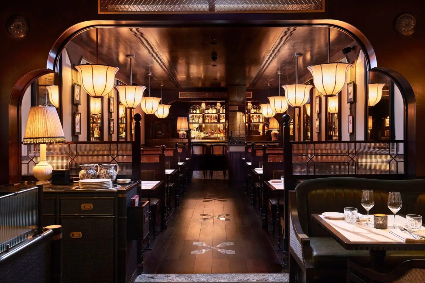 Gymkhana restaurant in london Dimly lit, elegant restaurant interior with warm lighting. Rows of tables lead to a central bar. Cosy ambiance with an upscale, classic feel. One of the best designed restaurants in london