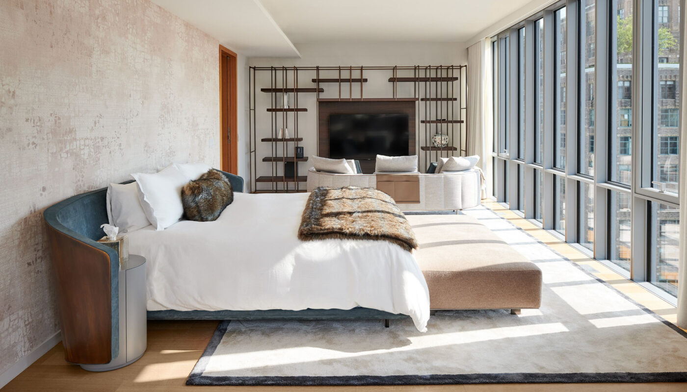 A serene bedroom by one of the influential Hispanic interior designers with a comfortable bed, a chair, a television, and a window providing a view outside.