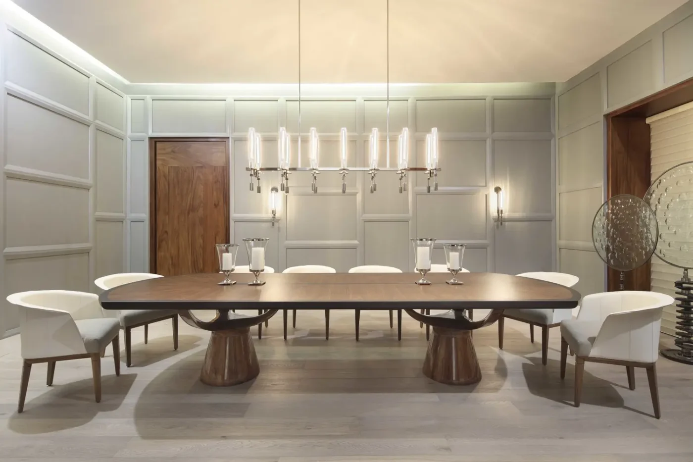 Lamzo-Design.jpg Modern dining room with a large wooden table, eight white chairs, and a sleek chandelier. Neutral colours create a calm and elegant atmosphere.