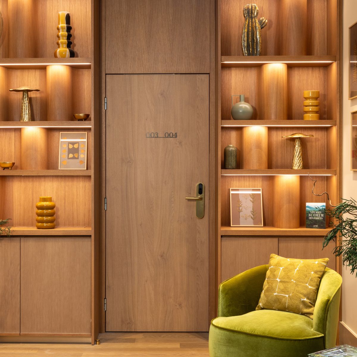 Le Cardinal Paris Hotel by Domkapa (2) Interior view of a room with wooden shelves and a green armchair, creating a cosy and inviting atmosphere.