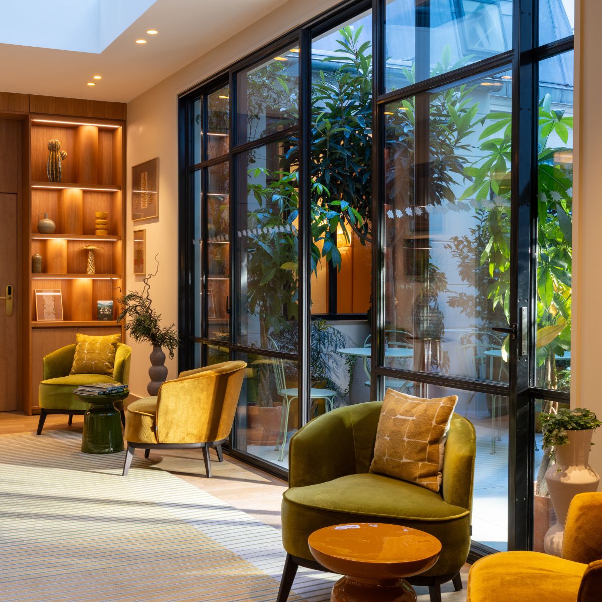 Le Cardinal Paris Hotel by Domkapa (3) Le Cardinal Paris Hotel lobby featuring bright green armchairs and lush green plants, creating a welcoming and vibrant atmosphere.