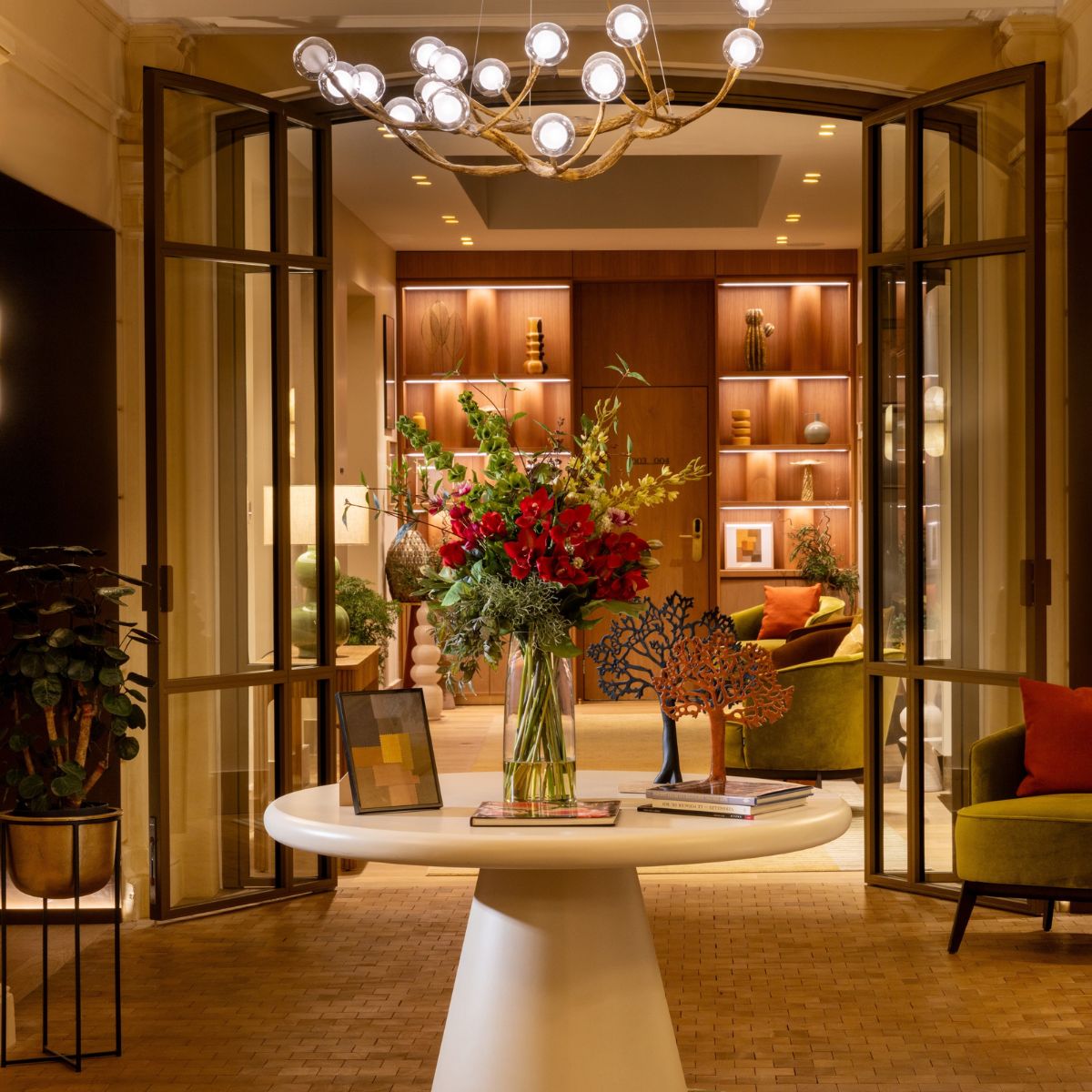 Le Cardinal Paris Hotel by Domkapa The lobby of a hotel adorned with a grand chandelier and colourful flowers, enhancing the space's elegance and charm.
