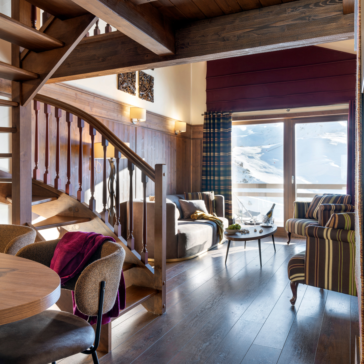 Cosy wooden stairs leading up in a warm, inviting room filled with natural light. A suite from the Le Hameau du Kashmir, a hotel in the French Alps.