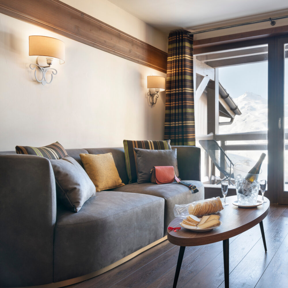 Bright living room scene showcasing a soft sofa, a chic table and a large window inviting sunlight inside. From Le Hameau du Kashmir hotel in the french alps.