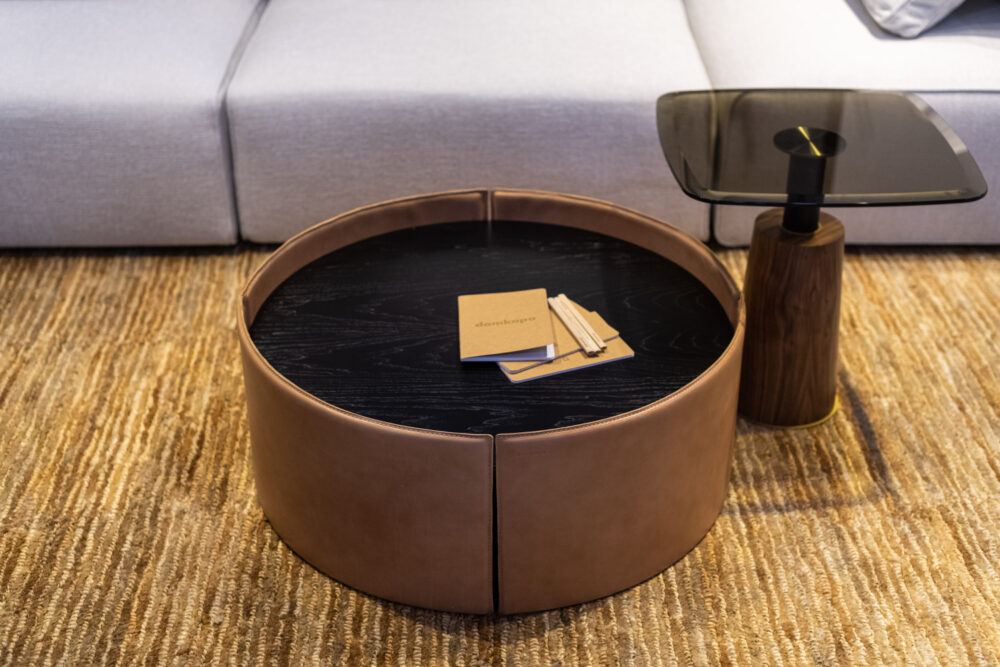 A coffee table upholstered in leather and with a top in dark wood showcased at a design fair.