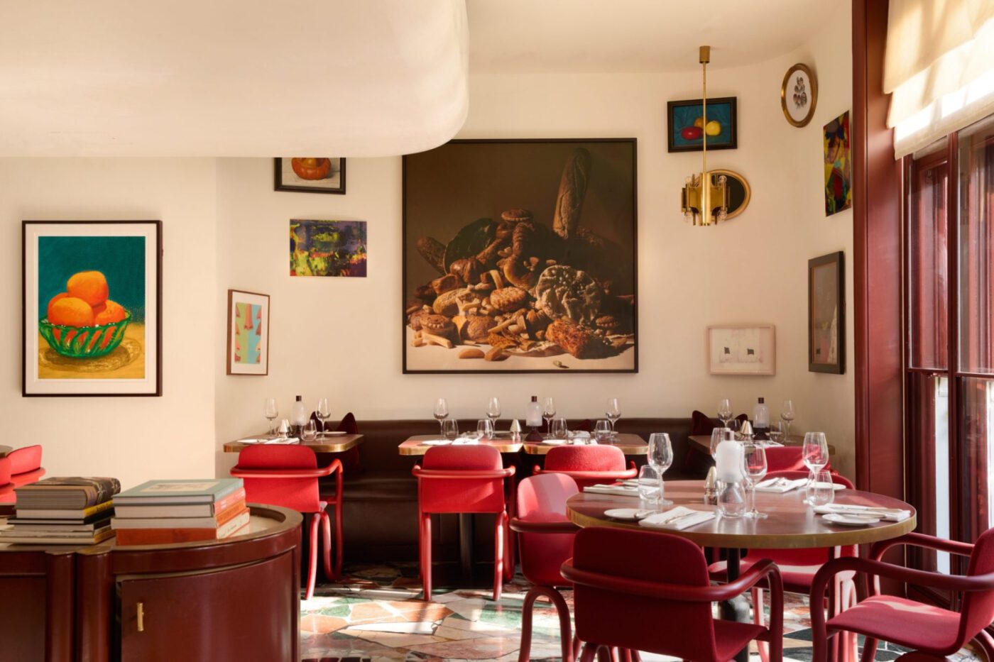 MountStreet_0172_london Chic restaurant interior with vibrant red chairs, elegant table settings, and diverse wall art. Sunlight streams through large windows, creating a warm, inviting atmosphere. One of the best designed restaurants in London.