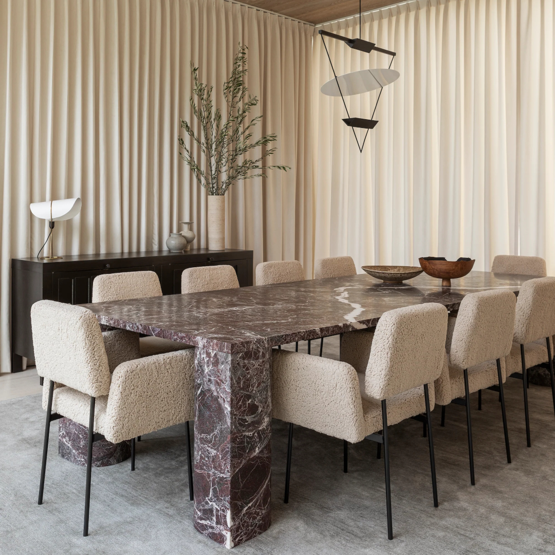 Dining room design with ten dining chairs in a bege boucle fabric and black steel legs. With a brown stone dining table and a black cabinet on the side.