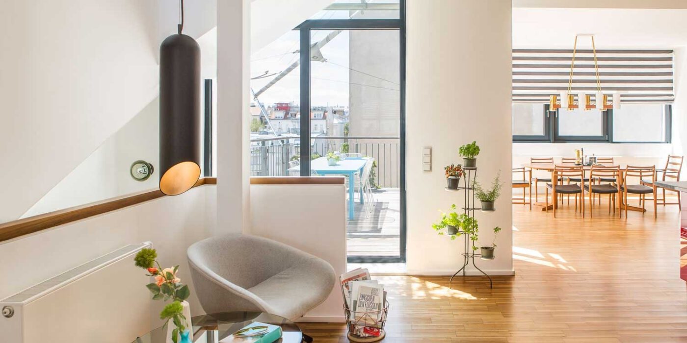 PHNeubau_01_by Christian Hantschel A modern living room with a stylish table and four chairs, accented by decorative items and a welcoming atmosphere.