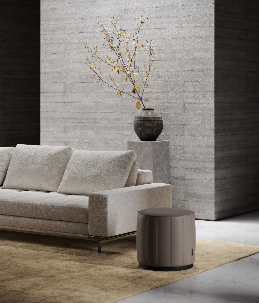 Modern industrial interior design living room with beige sofa, textured brick walls, vase with branches, and a round pouf in upholstered in brown leather.