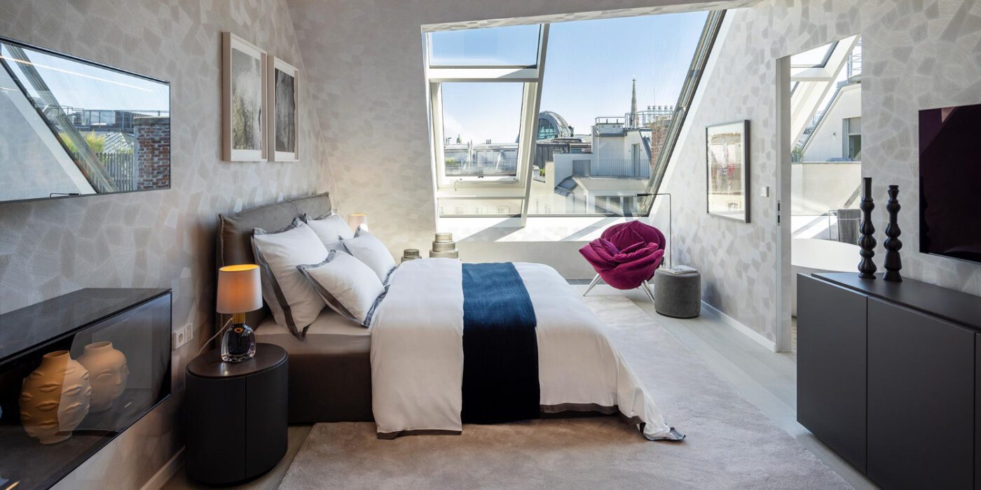 Penthouse_Opernring-by-frech-interior-design (1) A well-furnished bedroom with a large bed and a wall-mounted television, creating a comfortable atmosphere.