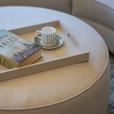 Rachel pouf in white with a book and a coffee cup on top.