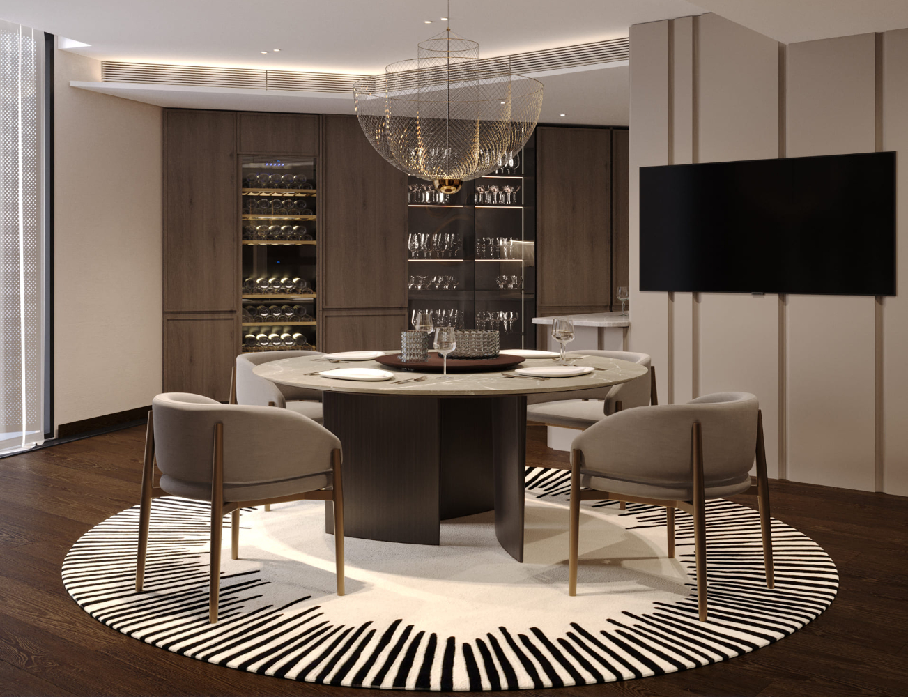 A modern dining room with a round table surrounded by four chairs on a patterned rug. A wine cabinet and shelves with glassware are in the background. A large chandelier hangs from the ceiling, and a flat-screen TV is mounted on the wall.