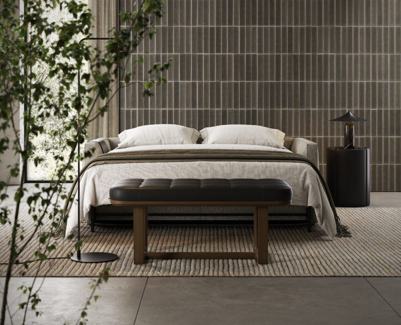 A modern bedroom with a neatly made bed, white pillows, and a dark gray blanket. A wooden bench is at the bed's foot, and a small round table with a lamp is on the side. A plant is in the foreground, and vertical tile walls and a large window are visible.