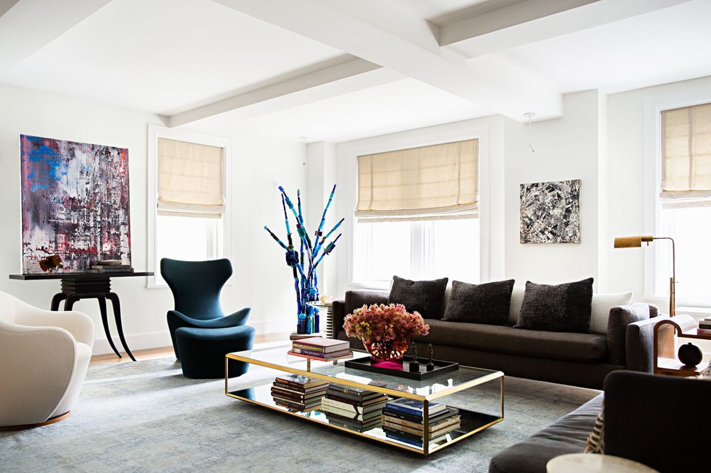 Living room design by Danielle Colding Design. With a sofa with brown tones and a blue armchair. The coffee table is in glass and gold accents.