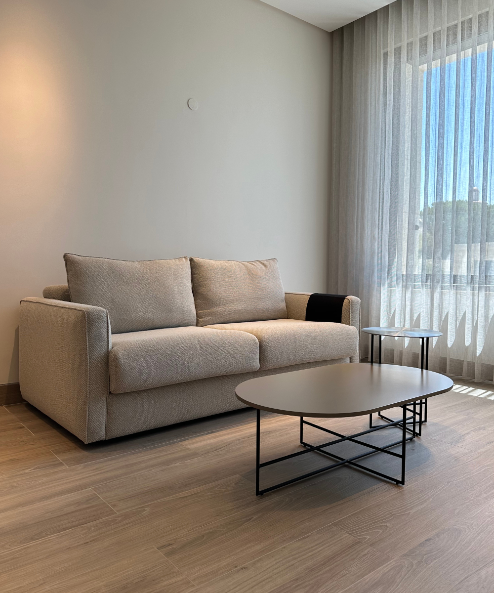 A bright living room in a bedroom with a comfortable sofa, a coffee table, and a window that offers a view outside. Project by Etch & Notch.
