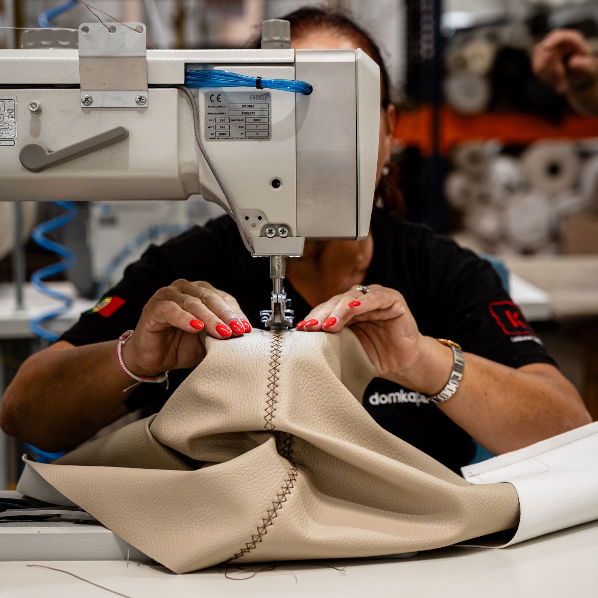 blog article about com vs house fabric by domkapa (5) A woman sews fabric on a sewing machine, demonstrating skill and attention to detail in her craft.