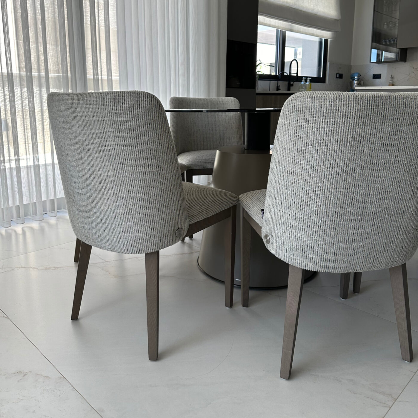 A round table featuring a glass surface, with four dining chairs positioned around it in a stylish setting. By Etch & Notch Designs.