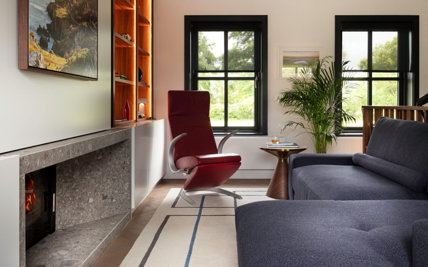 A warm living room scene with a navy blue modular sofa, a red armchair, a fireplace, and an artistic painting above the mantel.