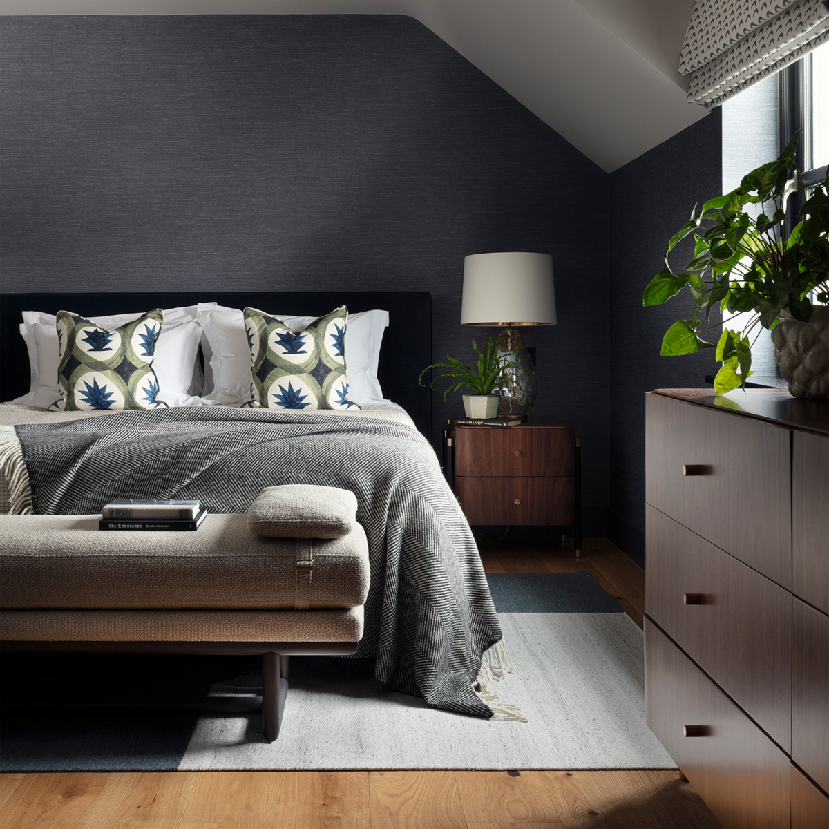 A contemporary bedroom showcasing dark walls and a well-arranged bed and a bench, offering a tranquil and inviting space. Designed by Edit Design Studio.