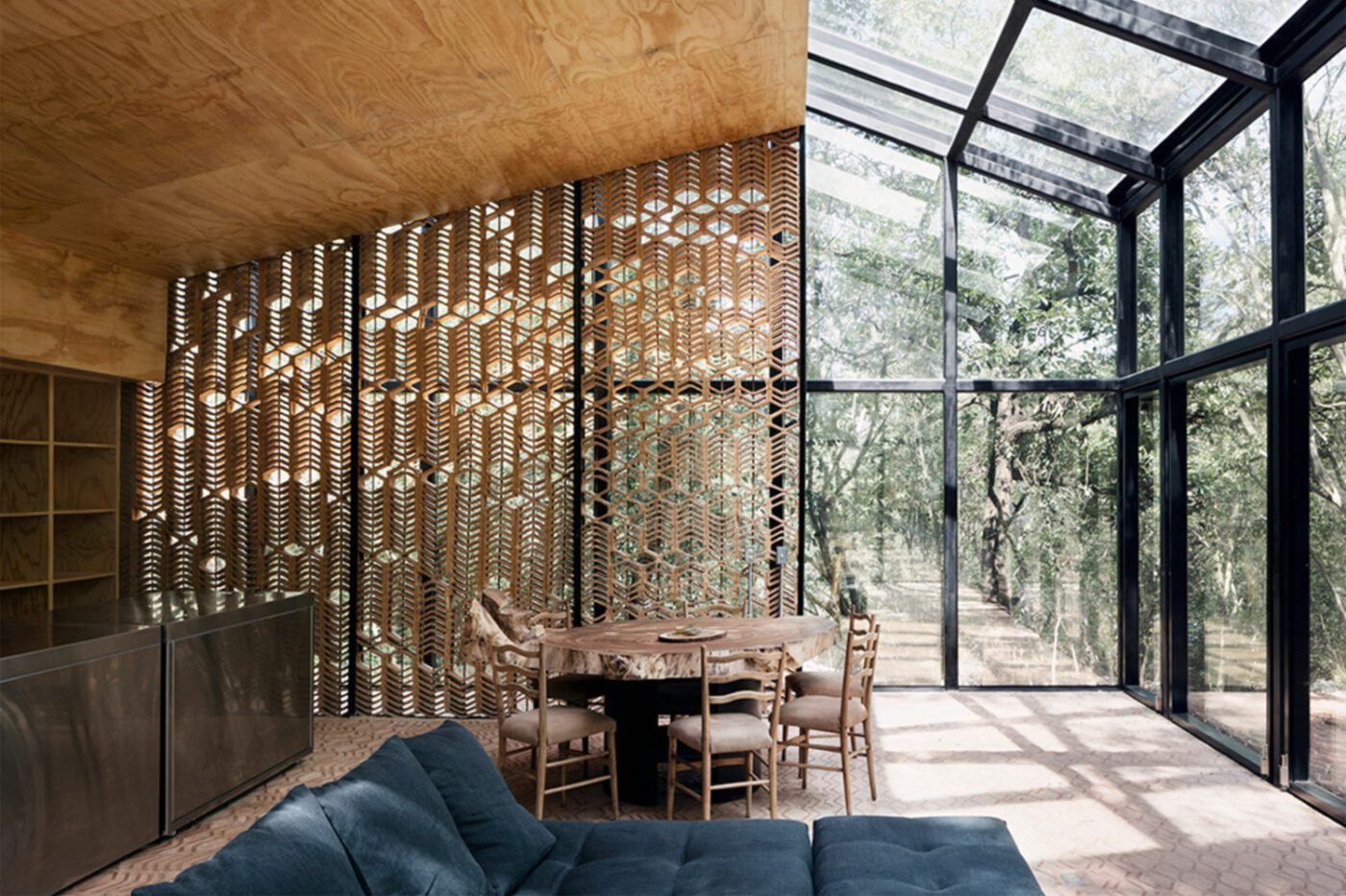 imgi_11_tatianabilbao-estudio-los-terrenos-house-san-pedro-garza-garcia-monterrey-rory-gardiner-04 Stylish modern interior with a blue sofa, wooden lattice wall, and glass ceiling overlooking trees. The space feels airy and connected to nature.