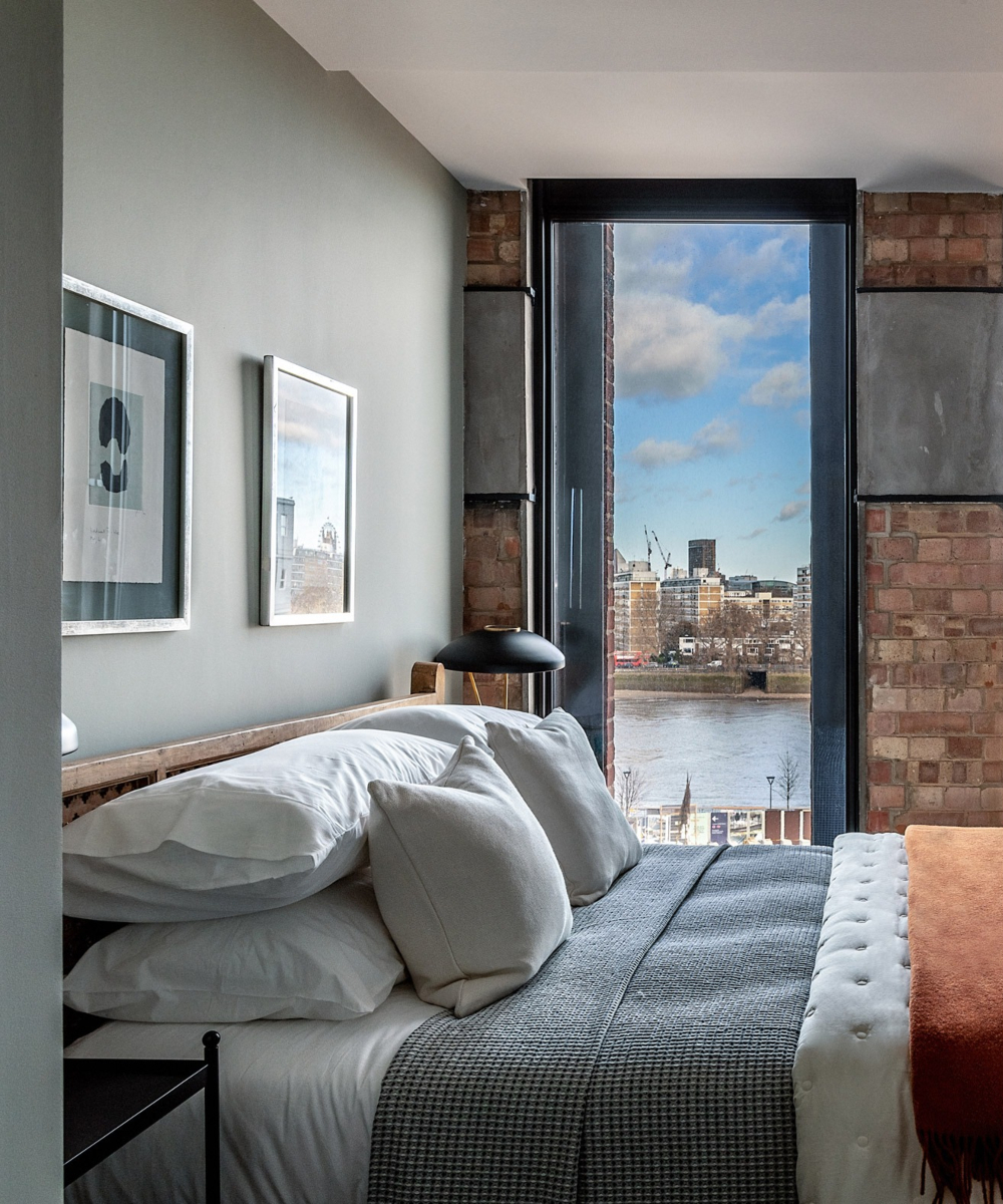A modern bedroom with a stunning cityscape visible from the large window. By Michaelis Boyd.