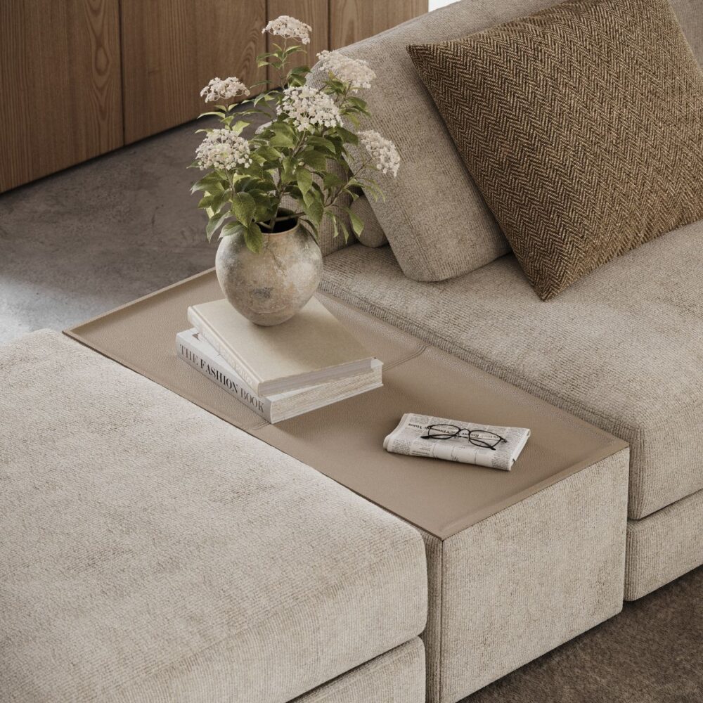 interior design trends for spring 2026 (2) A cosy beige moduçar sofa features a vase of white flowers, a book, and glasses on a side table. A brown patterned cushion adds warmth. Interior design trends for spring 2026
