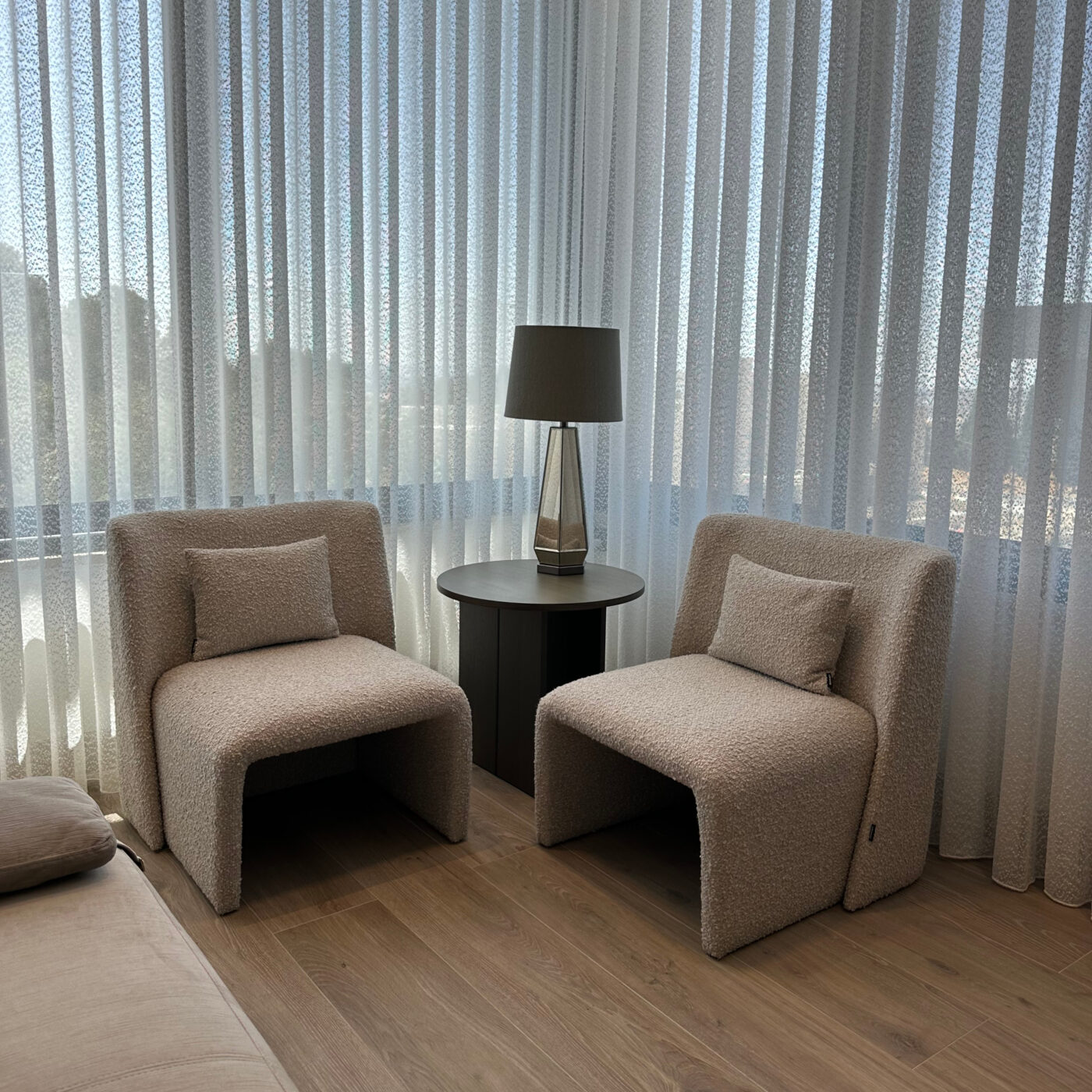 Two elegant armchairs in boucle placed in front of a window, draped with curtains, enhancing the room's inviting ambiance. Project by Etch & Notch Design's.