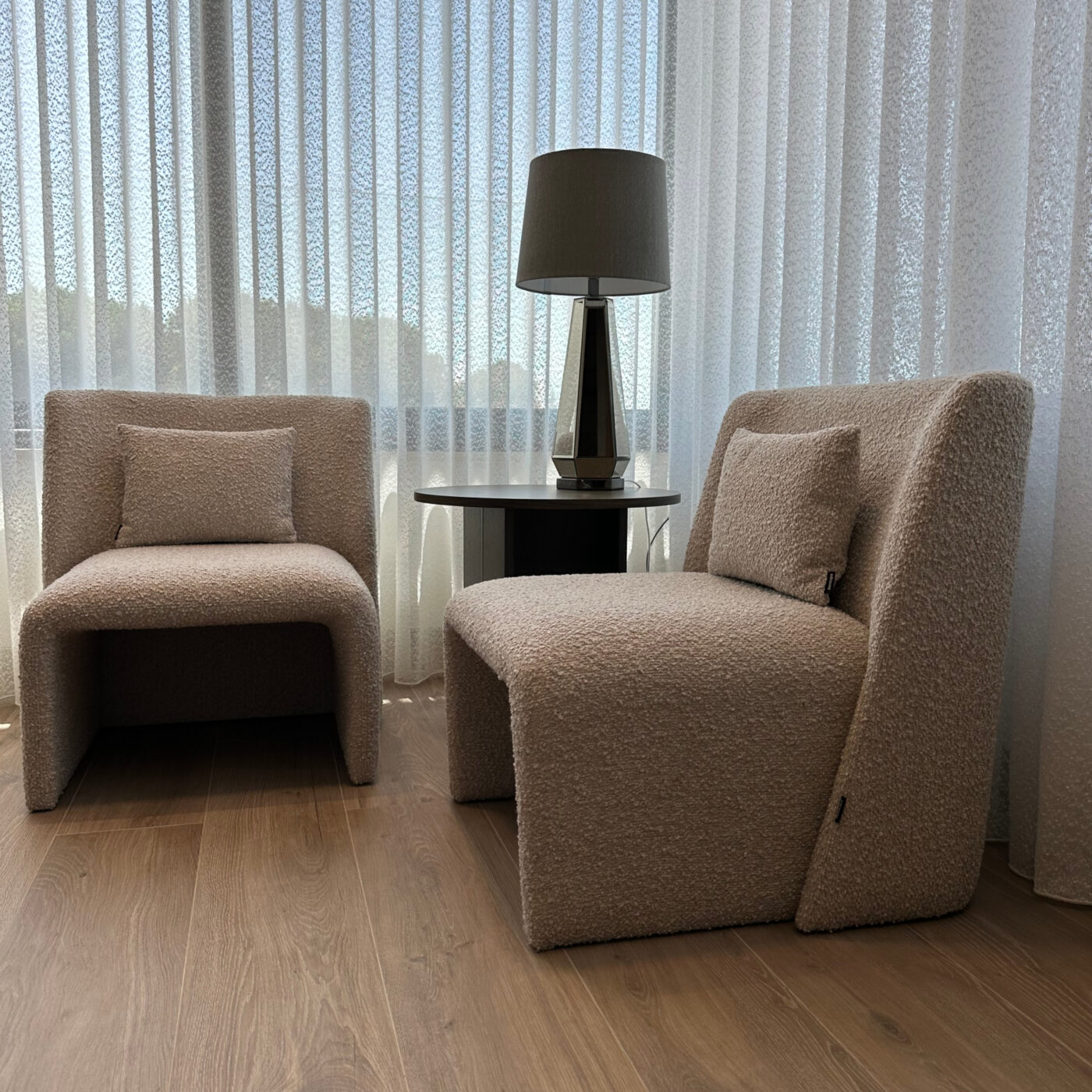 Two elegant armchairs in boucle placed in front of a window, draped with curtains, enhancing the room's inviting ambiance. Project by Etch & Notch Design's.