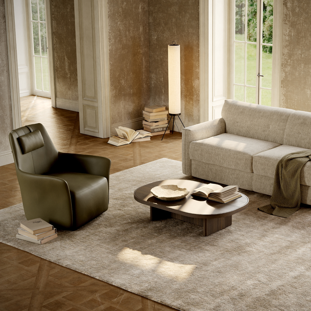 A cosy living room featuring a sofa bed, armchair, coffee table, lamp, and a decorative rug.