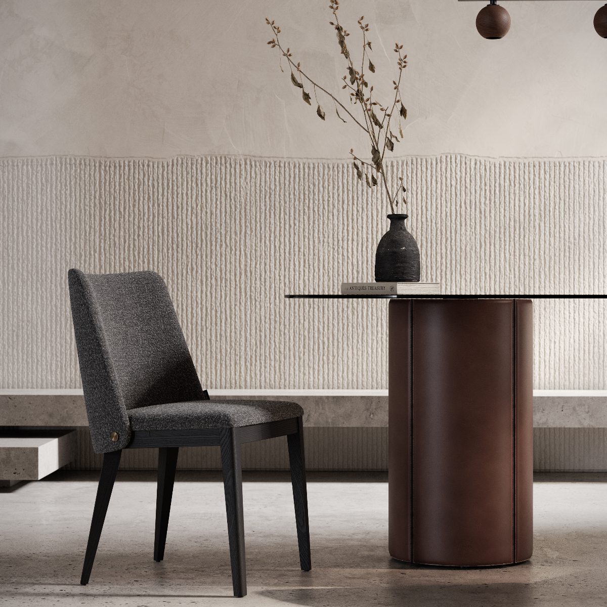 louise dining chair and mano dining table oval A modern dining area with a sleek dark grey dining chair and a round table. The table has a leather base and a book with a vase holding dried branches. The setting is minimalist and calm.