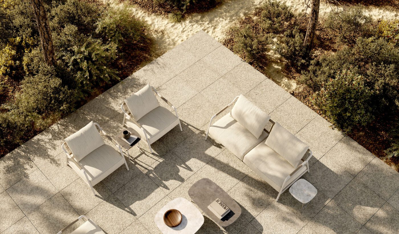 outdoor project by domkapa Modern outdoor patio with two cushioned armchairs, a sofa and two tables on a tiled surface. Surrounded by lush greenery and sunlight, conveying relaxation.