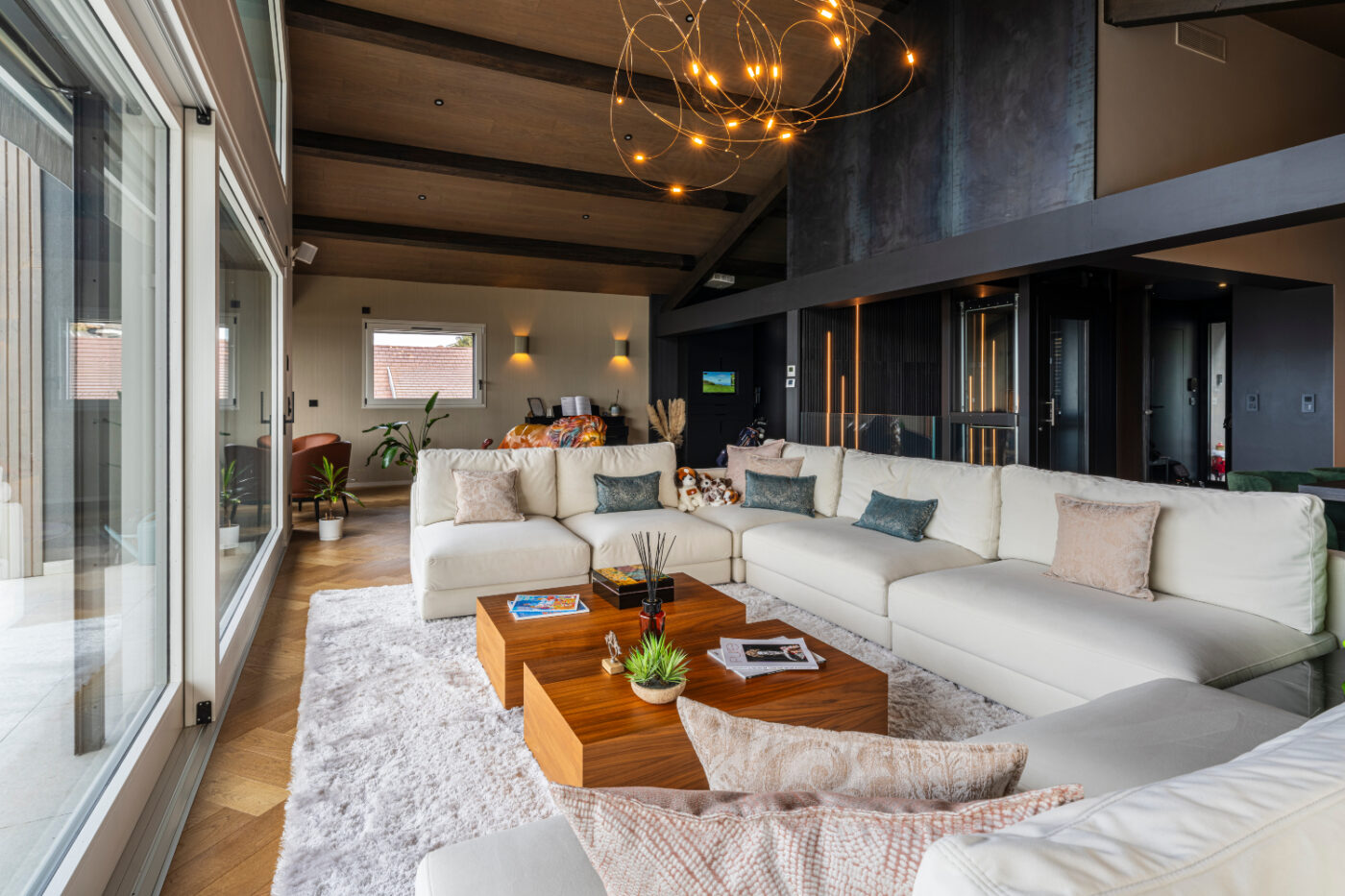 A modern living room by Aloona Design with sleek white furniture and a spacious glass door that opens to the outside. At the Villa "Du Lac" Project.