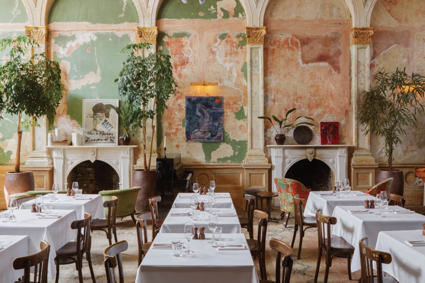 sessions art club in london Chic restaurant interior in London with vintage charm. Features distressed green and peach walls, ornate fireplaces, plants, and tables set with white linens.