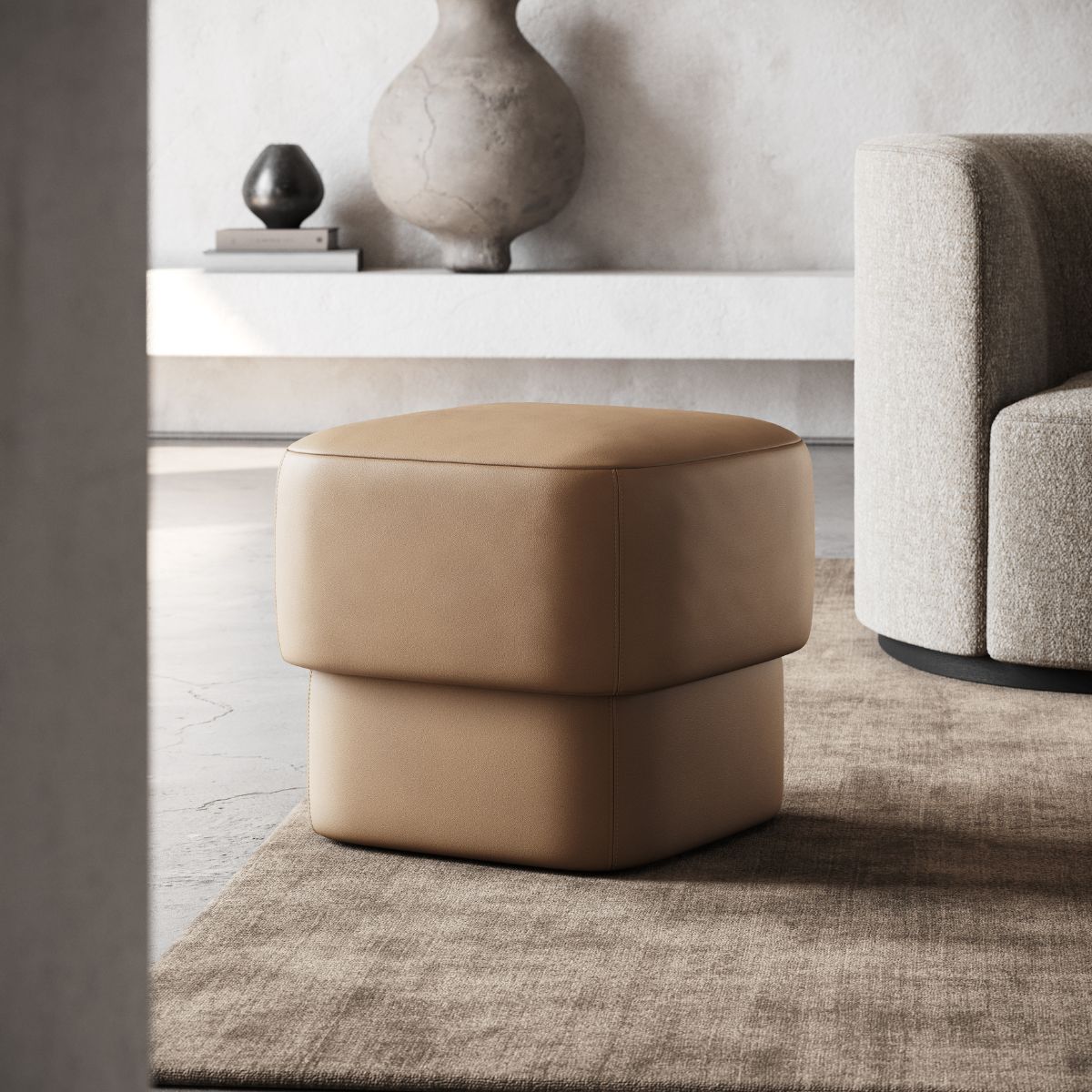 upholstered poufs selection (4) Modern interior with a minimalist, tan leather pouf on a beige rug. Nearby is a light gray sofa and a shelf with decorative vases, creating a calm ambiance.